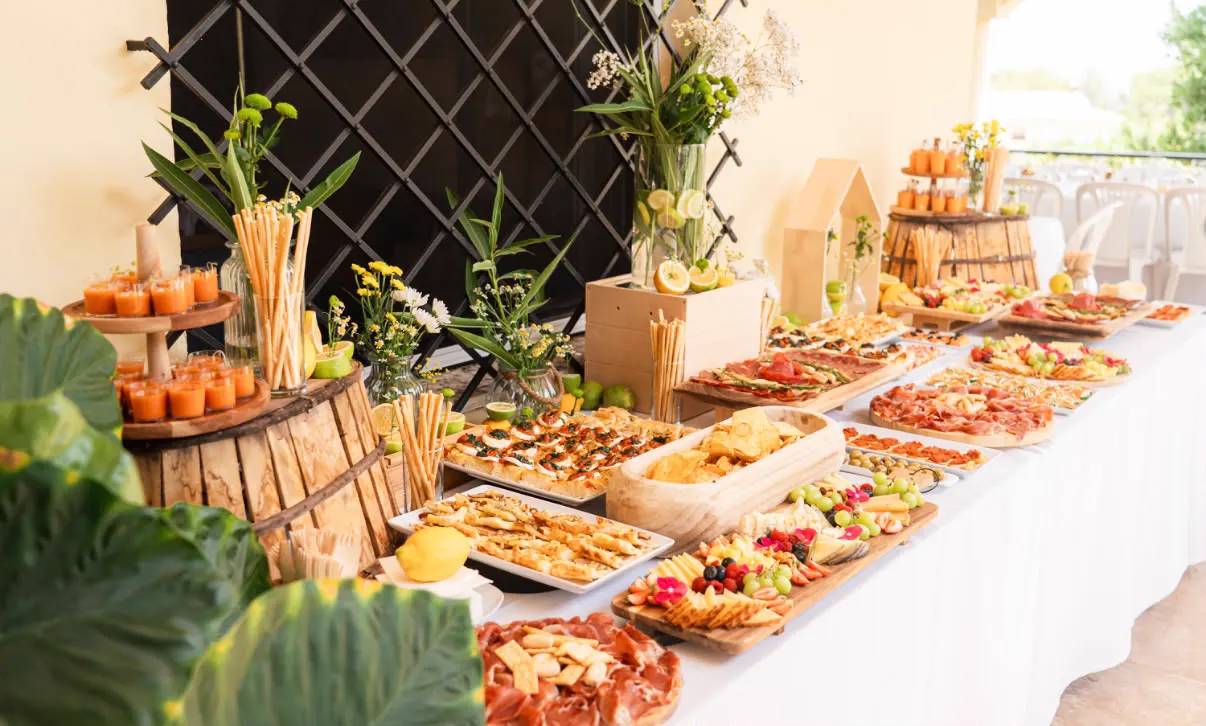 Mesa de catering con tablas de embutidos, quesos, fruta y aperitivos