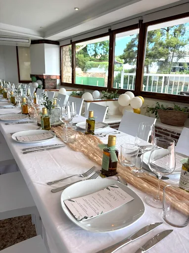 Mesa de boda con mantel blanco, botellas de aceite de regalo y caminos de lino